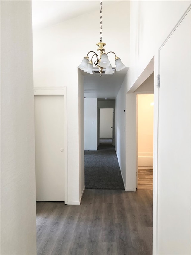 hallway with an inviting chandelier, dark wood-type flooring, and high vaulted ceiling