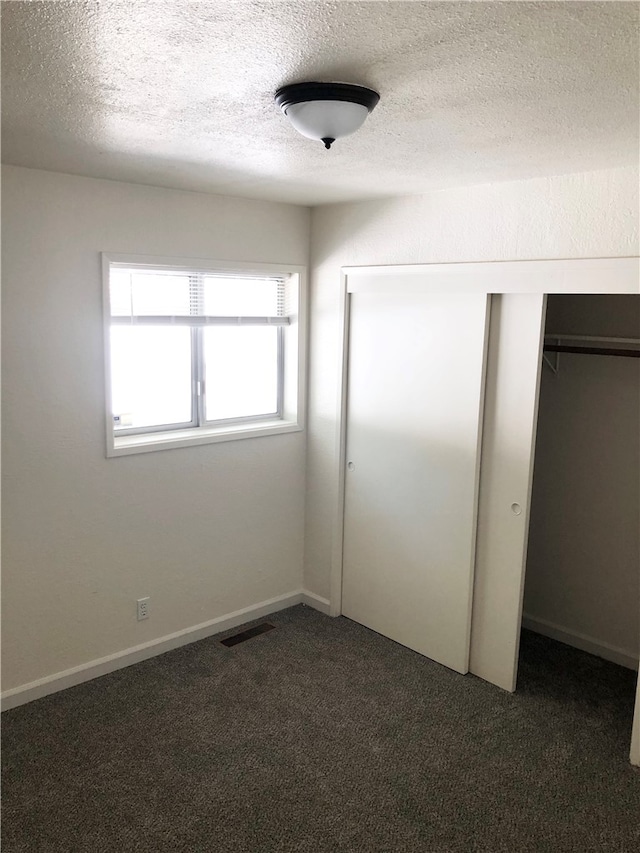 unfurnished bedroom featuring dark carpet, a textured ceiling, and a closet