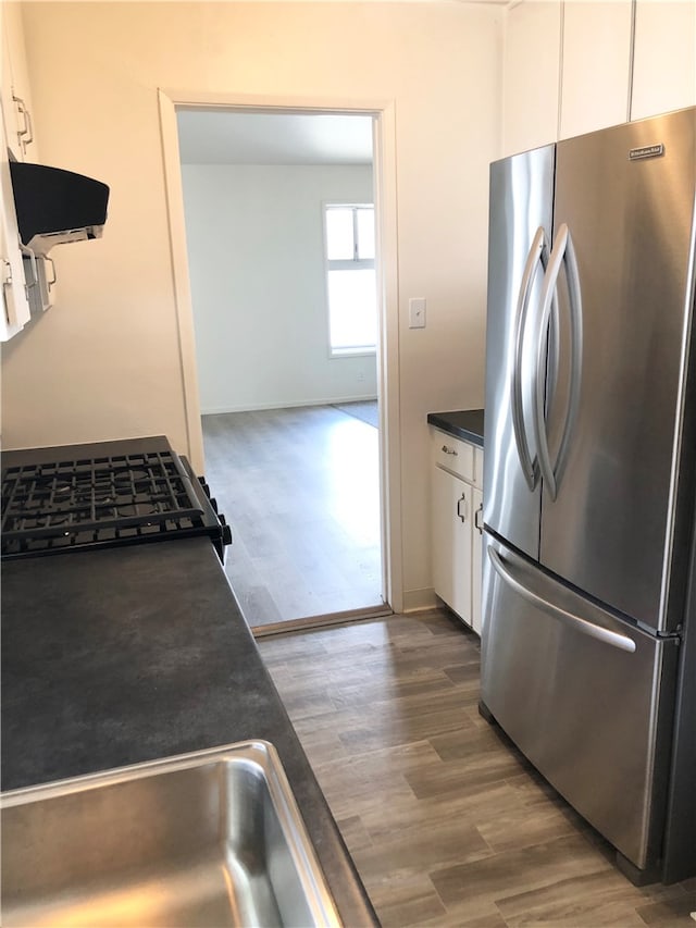 kitchen with white cabinetry, stainless steel refrigerator, dark hardwood / wood-style flooring, ventilation hood, and sink