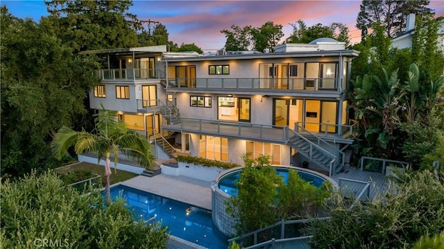 back house at dusk featuring a patio area and a balcony