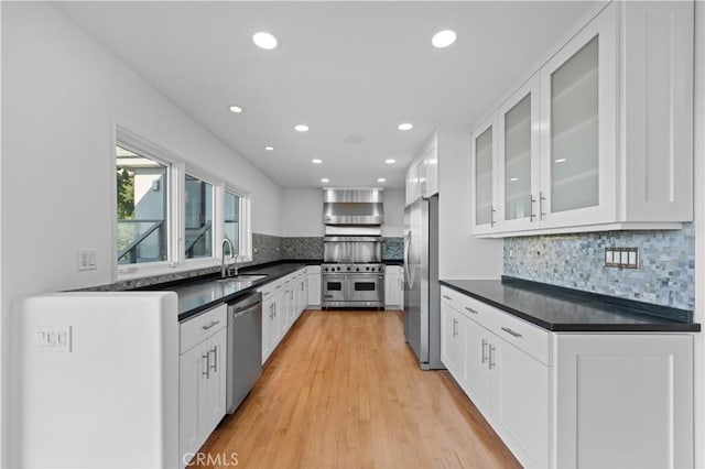 kitchen featuring sink, white cabinetry, light hardwood / wood-style flooring, stainless steel appliances, and wall chimney range hood