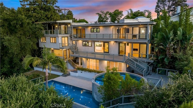 back of property at dusk with stairs, stucco siding, a balcony, a jacuzzi, and a patio