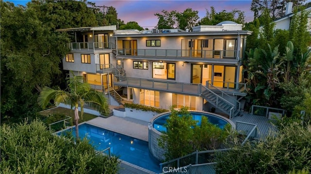 back of property at dusk with stairs, a patio, a balcony, and stucco siding