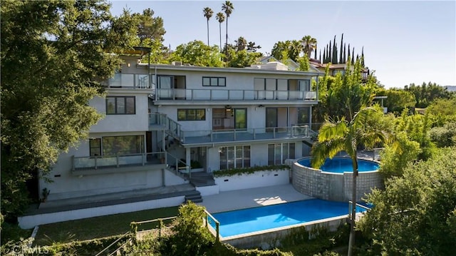 rear view of house with a balcony, stucco siding, an outdoor pool, and a patio