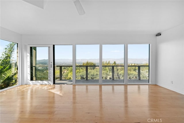 unfurnished room with wood finished floors, a mountain view, and ceiling fan