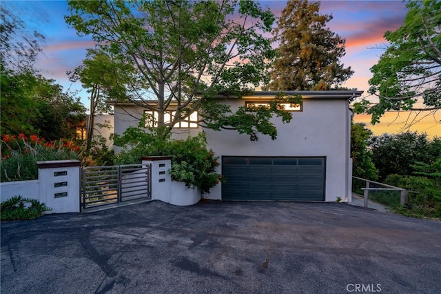 view of front of property featuring a gate, fence, driveway, stucco siding, and a garage