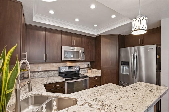 kitchen with sink, decorative light fixtures, appliances with stainless steel finishes, a tray ceiling, and light stone countertops