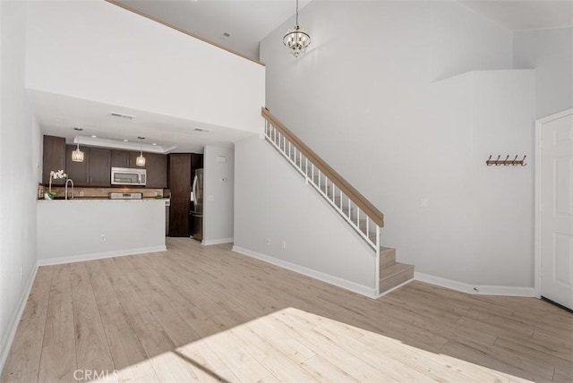 unfurnished living room with sink, a towering ceiling, light hardwood / wood-style flooring, and a chandelier