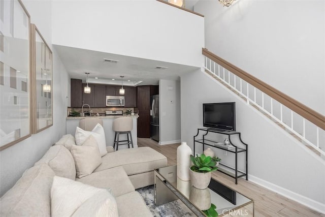 living area featuring baseboards, visible vents, a towering ceiling, stairway, and light wood-style floors