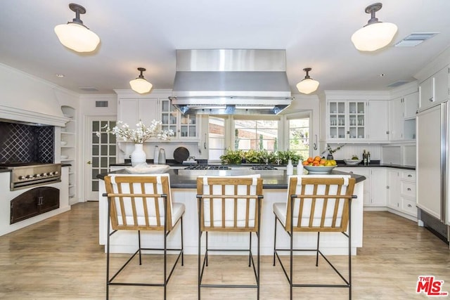 kitchen with hanging light fixtures, white cabinetry, range hood, a breakfast bar area, and light hardwood / wood-style floors