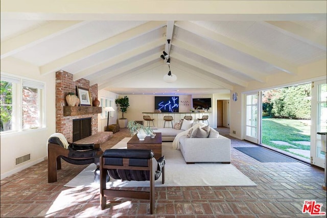 living room with a brick fireplace, lofted ceiling with beams, and a wealth of natural light