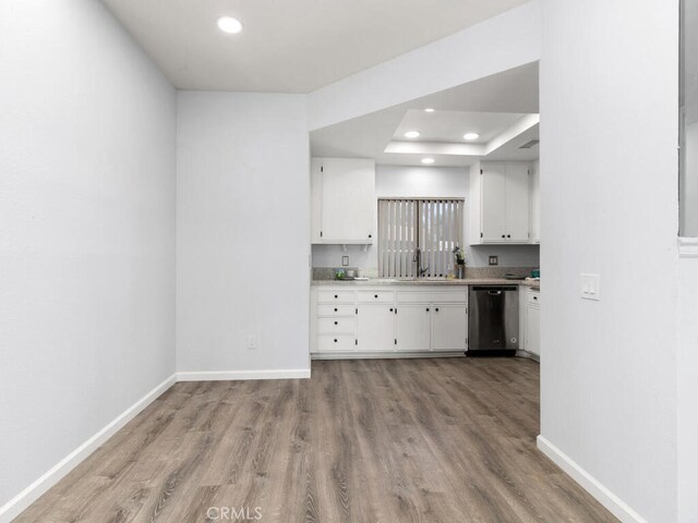 kitchen with a tray ceiling, sink, white cabinets, light hardwood / wood-style flooring, and stainless steel dishwasher