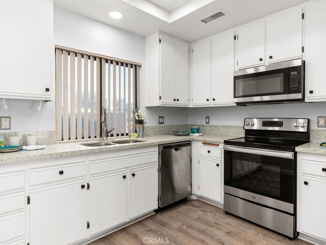 kitchen featuring white cabinets, stainless steel appliances, light wood-type flooring, and sink