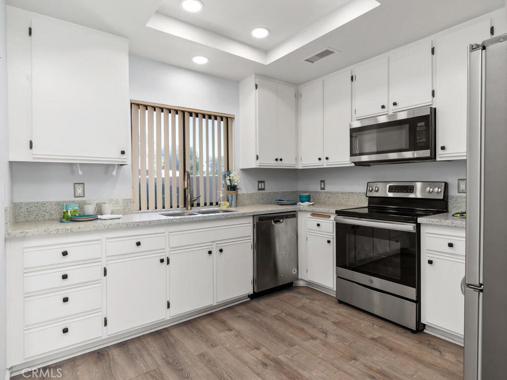 kitchen with white cabinets, a raised ceiling, sink, stainless steel appliances, and light hardwood / wood-style floors