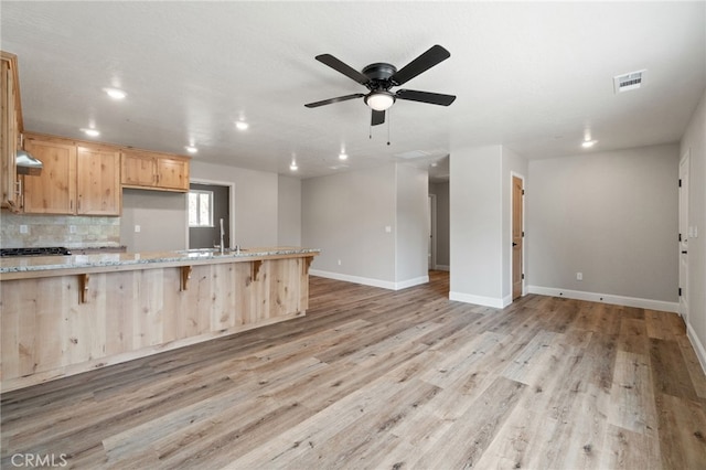 kitchen with light stone counters, light brown cabinets, range hood, a breakfast bar, and light hardwood / wood-style floors