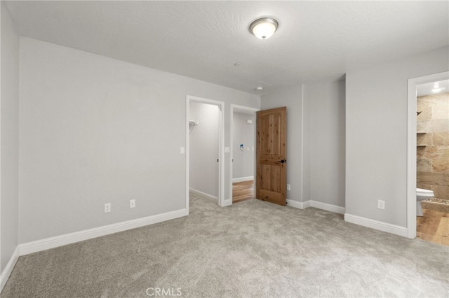 unfurnished bedroom with a spacious closet, light carpet, ensuite bathroom, and a closet