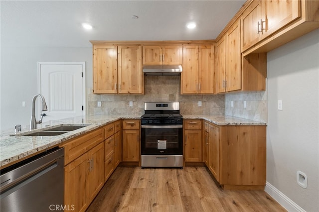 kitchen with light wood-type flooring, sink, tasteful backsplash, stainless steel appliances, and light stone countertops