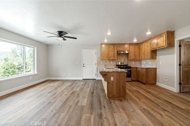 kitchen featuring light wood-type flooring, sink, a center island with sink, stainless steel range oven, and light stone countertops