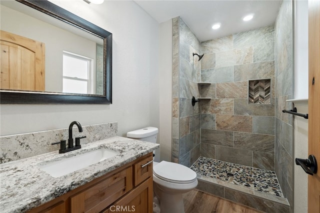 bathroom with tiled shower, hardwood / wood-style floors, vanity, and toilet