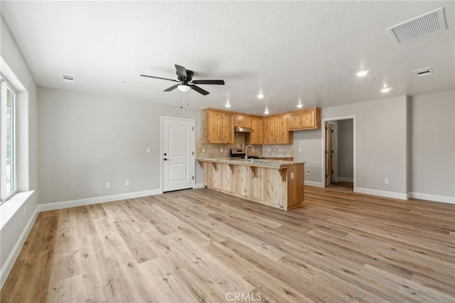 kitchen featuring a kitchen island with sink, sink, light hardwood / wood-style flooring, decorative backsplash, and ceiling fan