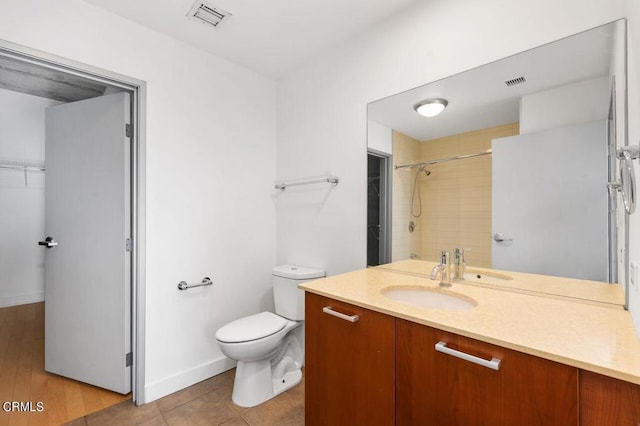 bathroom with wood-type flooring, vanity, a tile shower, and toilet