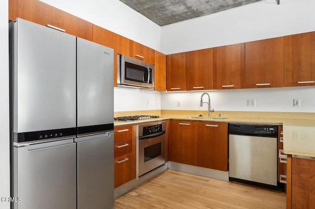 kitchen with sink, appliances with stainless steel finishes, and light hardwood / wood-style flooring