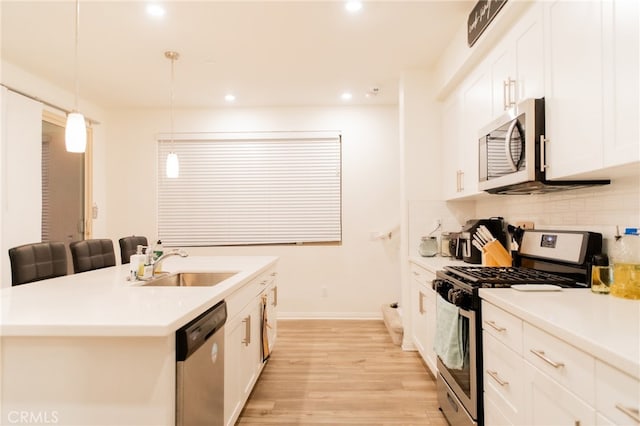 kitchen featuring white cabinets, hanging light fixtures, sink, appliances with stainless steel finishes, and light hardwood / wood-style floors