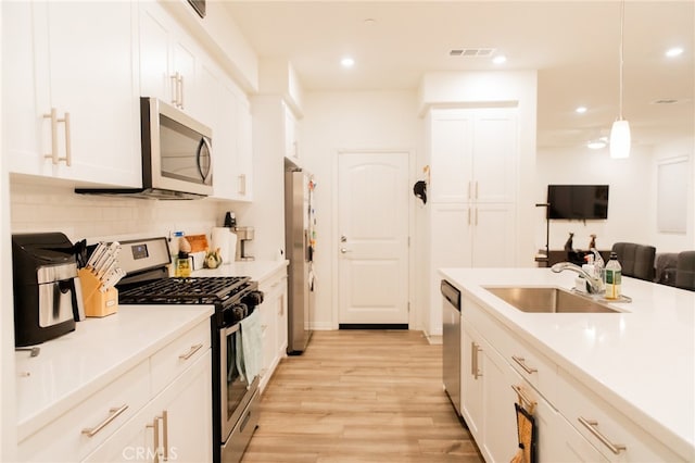 kitchen with pendant lighting, light wood-type flooring, sink, white cabinetry, and stainless steel appliances