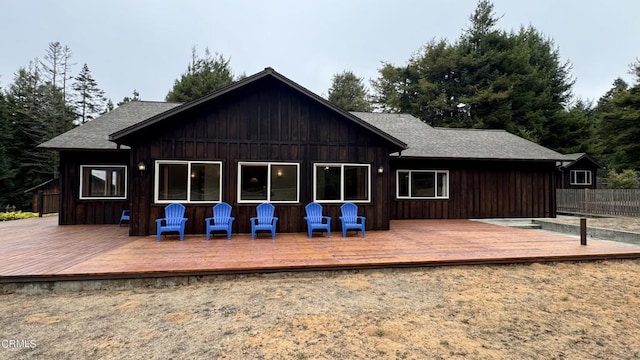 back of property with a shingled roof, fence, and a wooden deck