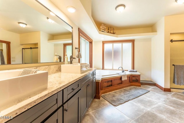 full bathroom with double vanity, a garden tub, baseboards, and a sink