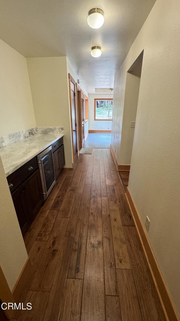 corridor with dark wood-style floors, beverage cooler, a textured ceiling, and baseboards