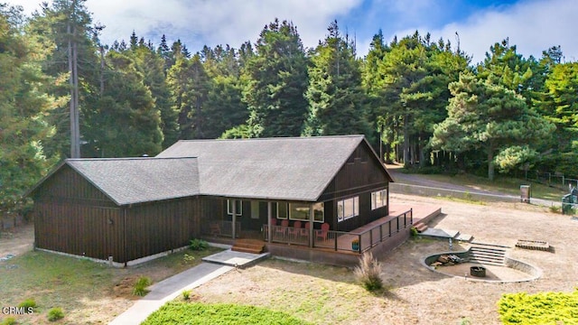view of front of property with a porch, a wooded view, and a shingled roof