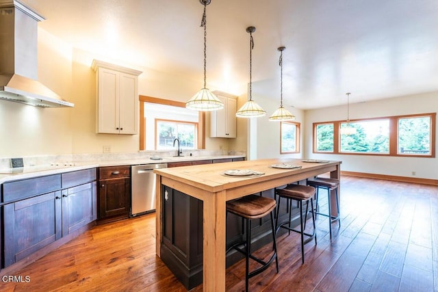 kitchen featuring wall chimney range hood, stainless steel dishwasher, butcher block counters, white stovetop, and a breakfast bar area