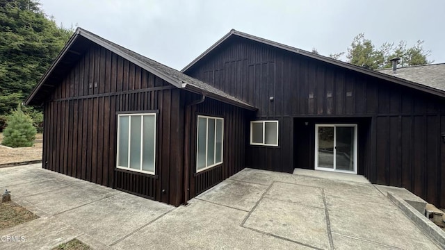 view of side of property with board and batten siding, a patio area, and roof with shingles