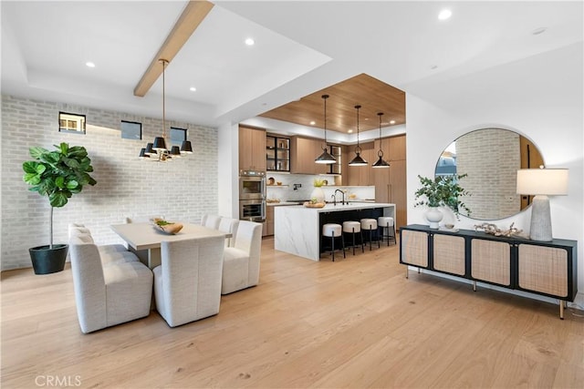 dining area with recessed lighting, a tray ceiling, light wood-style floors, and brick wall