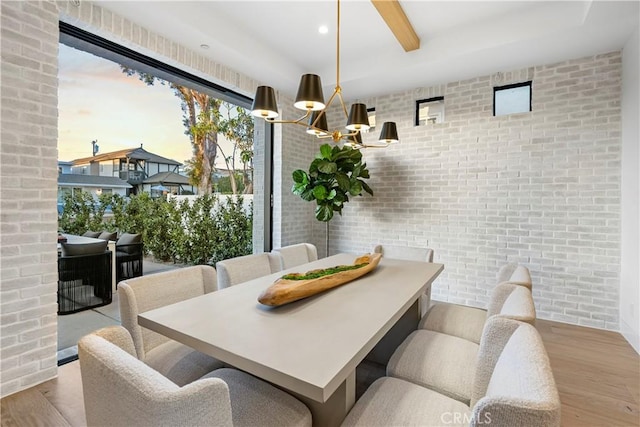 dining area featuring an inviting chandelier, wood finished floors, brick wall, and beam ceiling