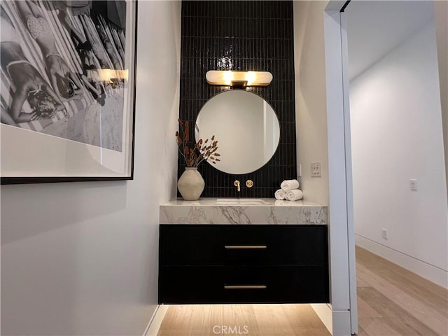 bathroom featuring vanity, wood finished floors, tasteful backsplash, and baseboards