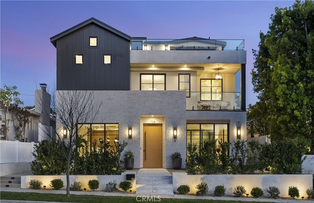 contemporary home featuring a balcony, fence, and brick siding