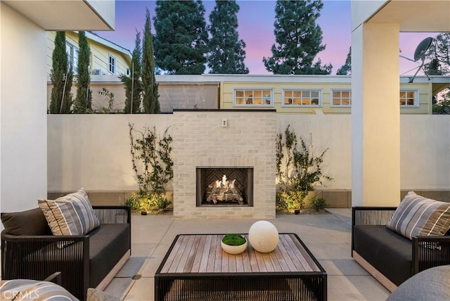 patio terrace at dusk with an outdoor living space with a fireplace and fence