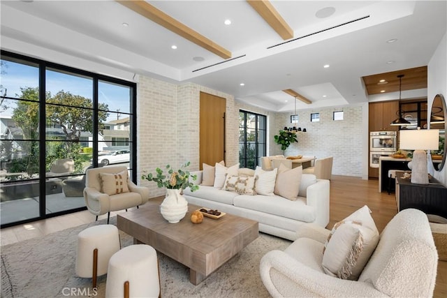 living room with brick wall, beam ceiling, light wood-style flooring, recessed lighting, and a raised ceiling