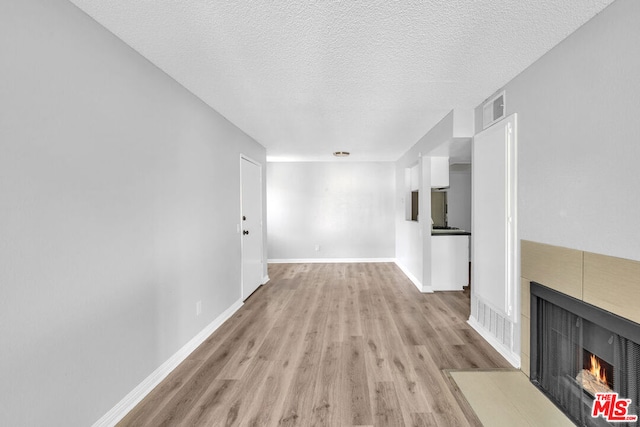 unfurnished living room featuring a textured ceiling, a fireplace, and light hardwood / wood-style flooring