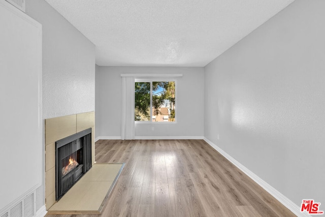 unfurnished living room with light wood-type flooring, a textured ceiling, and a tiled fireplace