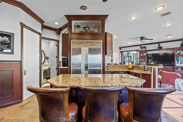 kitchen featuring light stone counters, kitchen peninsula, a kitchen island, paneled fridge, and crown molding