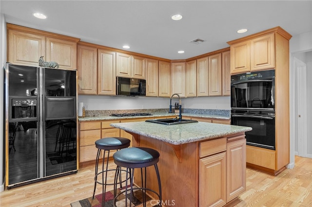 kitchen with light wood-type flooring, black appliances, sink, and an island with sink