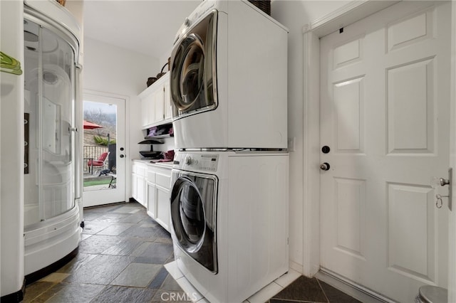 clothes washing area featuring cabinets and stacked washing maching and dryer