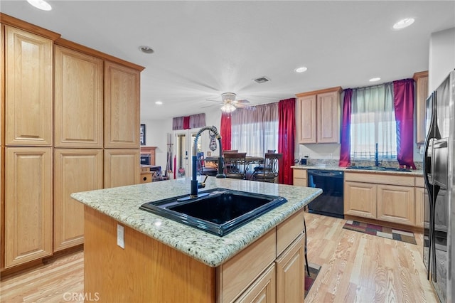 kitchen with ceiling fan, sink, a kitchen island with sink, black appliances, and light wood-type flooring