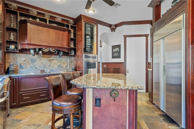 kitchen with light stone counters, backsplash, a center island, appliances with stainless steel finishes, and a breakfast bar