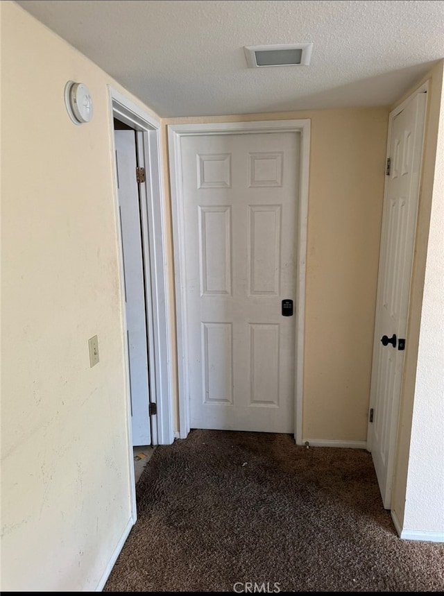 hall with dark carpet and a textured ceiling