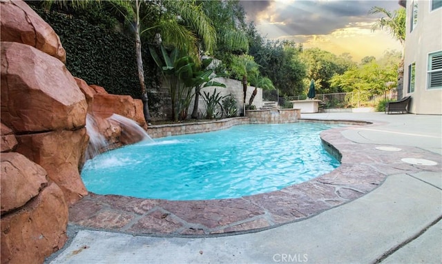 pool at dusk with pool water feature and a hot tub