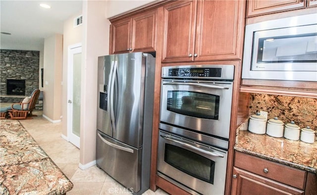 kitchen with stone counters, light tile patterned flooring, a stone fireplace, and appliances with stainless steel finishes